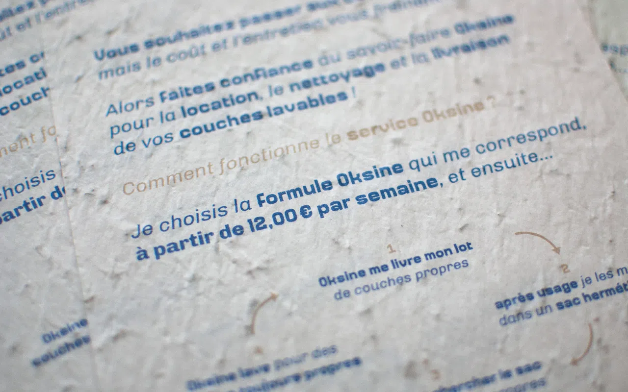 Photographie du flyer A5, permettant de découvrir la texture du papier ensemencé et le travail typographique.